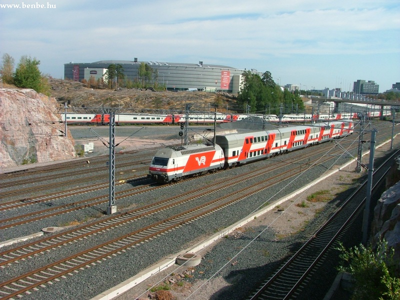 An InterCity2 train with an Sr2 type locomotive is running to Turku near Ilmala with a Pendolino exiting Ilmala depot in the background photo